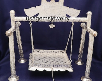 May include: A silver-colored decorative swing with intricate patterns and a detailed top design. The swing is suspended by chains from a horizontal bar supported by four vertical posts. The text "usagemsjewelry" is visible on the horizontal bar.