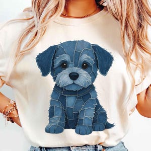 May include: Cream-colored t-shirt featuring a blue denim patchwork puppy design. The puppy has large, expressive eyes and a denim collar. The design is centered on the shirt, creating a playful and casual look.