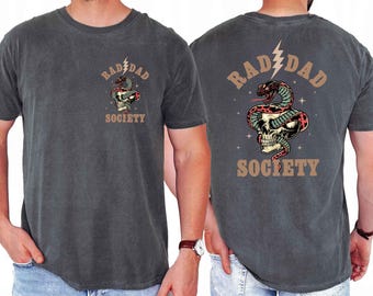 May include: A dark gray t-shirt with a vintage-style graphic of a skull with a snake wrapped around it. The text "RAD DAD SOCIETY" is printed in brown above and below the graphic.
