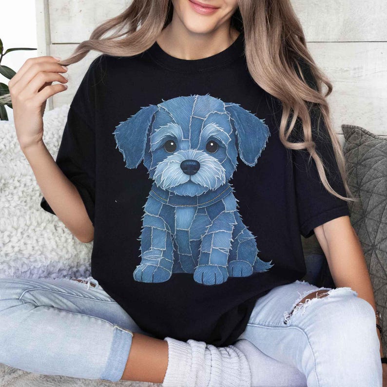 May include: Black t-shirt featuring a blue denim-style puppy illustration. The puppy is sitting, with a light blue nose and white accents. The design is centered on the shirt.