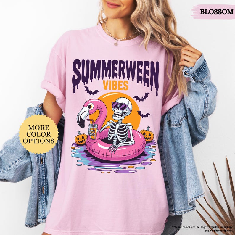 K&ouml;nnte beinhalten: Hellrosa T-Shirt mit einem farbenfrohen Motiv. Es zeigt ein Skelett mit Sonnenbrille auf einem rosa Flamingo-Schwimmer, dar&uuml;ber steht "SUMMERWEEN VIBES". Flederm&auml;use und K&uuml;rbisse sind ebenfalls abgebildet. Der Text "MORE COLOR OPTIONS" ist sichtbar.
