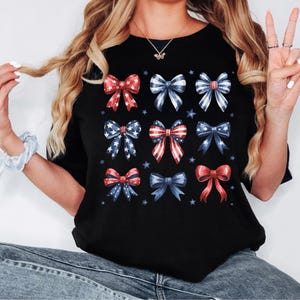 May include: Black t-shirt with a pattern of red, white, and blue bows. The bows are arranged in a grid pattern and have a vintage look.