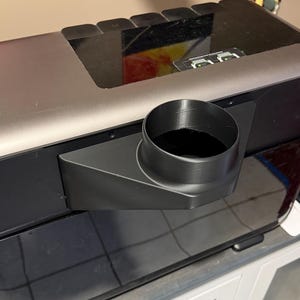 May include: A black and gray electronic device with a cylindrical outlet. The device has a rectangular shape with a silver top and a black base. The outlet is a black cylinder extending from the side.