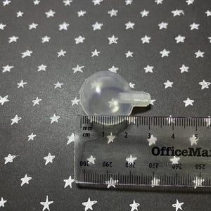 May include: A clear plastic ball with a small hole on the side, measuring approximately 2 cm in diameter. The ball is sitting on a black surface with white stars.