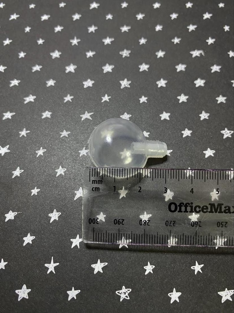 May include: A clear plastic ball with a small hole on the side, measuring approximately 2 cm in diameter. The ball is sitting on a black surface with white stars.