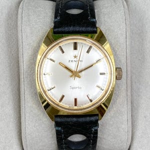 May include: A gold-toned Zenith Sporto watch with a white face, gold hands, and a black leather strap. The watch face displays the Zenith logo and the word "Sporto". The watch has a round face and a brown crown.