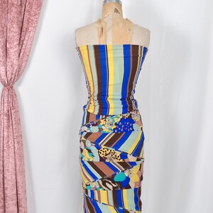 Puede incluir: Vestido sin tirantes y colorido sobre un maniqu&iacute;. El vestido presenta rayas verticales en azul, amarillo y marr&oacute;n en el corpi&ntilde;o, que se transforman en una falda estampada con dise&ntilde;os florales y geom&eacute;tricos. El vestido es fruncido y ajustado.