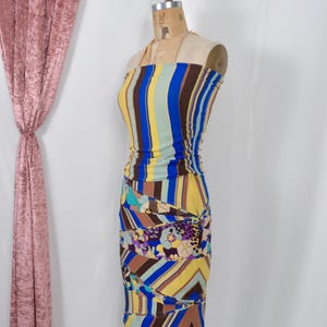 Puede incluir: Un vestido sin tirantes colorido con rayas verticales en azul, amarillo y marr&oacute;n. La parte inferior presenta un patr&oacute;n geom&eacute;trico y floral. El vestido se exhibe en un maniqu&iacute;, mostrando su dise&ntilde;o ajustado.