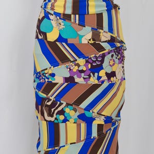 Puede incluir: Vestido estampado y colorido con silueta ajustada. El vestido presenta una mezcla de rayas verticales en amarillo, azul y marr&oacute;n, junto con dise&ntilde;os florales y abstractos. El vestido se exhibe en un maniqu&iacute;.