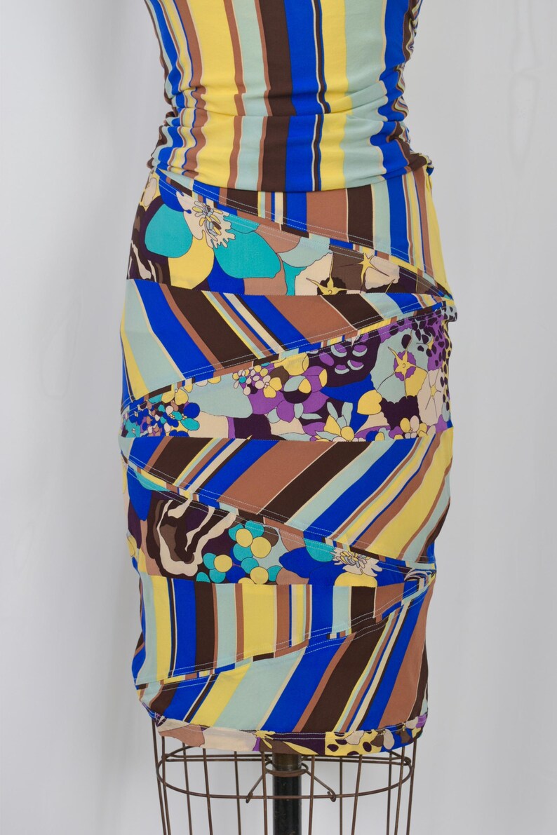 Puede incluir: Vestido estampado y colorido con silueta ajustada. El vestido presenta una mezcla de rayas verticales en amarillo, azul y marr&oacute;n, junto con dise&ntilde;os florales y abstractos. El vestido se exhibe en un maniqu&iacute;.