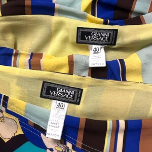 Puede incluir: Primer plano de tela colorida con rayas verticales en amarillo, azul, marr&oacute;n y turquesa. La tela tiene una etiqueta que dice "GIANNI VERSACE" y talla 40. La tela es probablemente parte de una prenda.