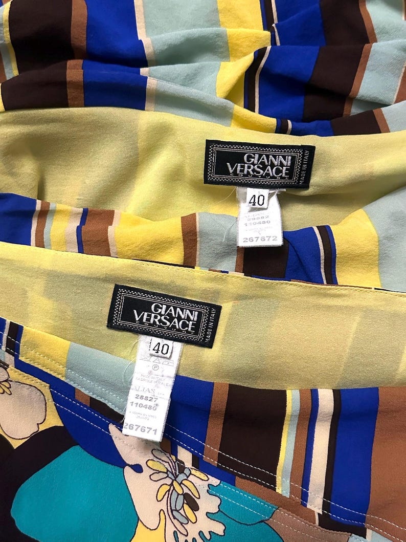 Puede incluir: Primer plano de tela colorida con rayas verticales en amarillo, azul, marr&oacute;n y turquesa. La tela tiene una etiqueta que dice "GIANNI VERSACE" y talla 40. La tela es probablemente parte de una prenda.