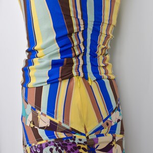 Puede incluir: Un vestido colorido y ajustado con rayas verticales azules, amarillas y marrones. La parte inferior presenta un estampado floral con detalles morados y beige. Una cremallera amarilla recorre el lateral.