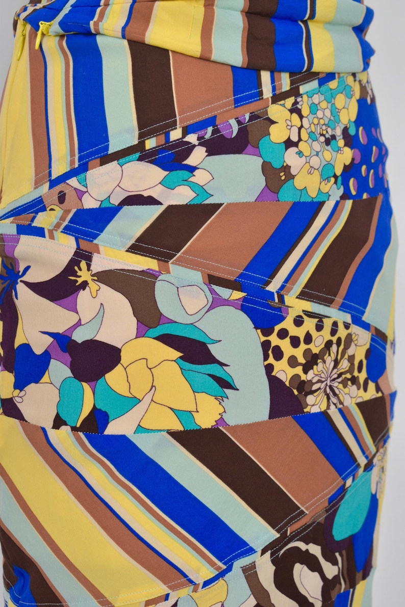 Puede incluir: Falda estampada con dise&ntilde;o patchwork. La falda presenta una vibrante mezcla de colores que incluyen amarillo, azul, marr&oacute;n y morado, con estampados florales y de rayas. La falda tiene una silueta ajustada.