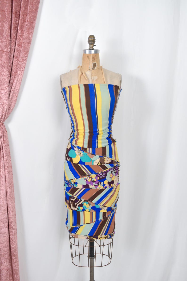 Puede incluir: Vestido vintage sin tirantes sobre un maniqu&iacute;. El vestido presenta rayas verticales en amarillo, azul, marr&oacute;n y verde. La parte inferior tiene un estampado floral y geom&eacute;trico. El vestido se exhibe en un maniqu&iacute; de alambre.