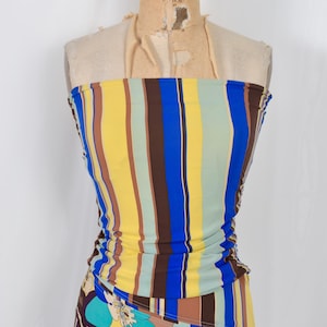 Puede incluir: Vestido sin tirantes sobre maniqu&iacute; con rayas verticales amarillas, azules, marrones y verdes. La parte inferior tiene un estampado floral con flores azules, moradas y amarillas. Ropa de verano.