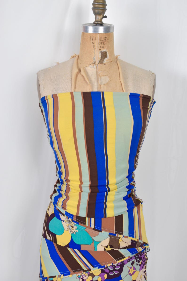 Puede incluir: Vestido sin tirantes sobre maniqu&iacute; con rayas verticales amarillas, azules, marrones y verdes. La parte inferior tiene un estampado floral con flores azules, moradas y amarillas. Ropa de verano.
