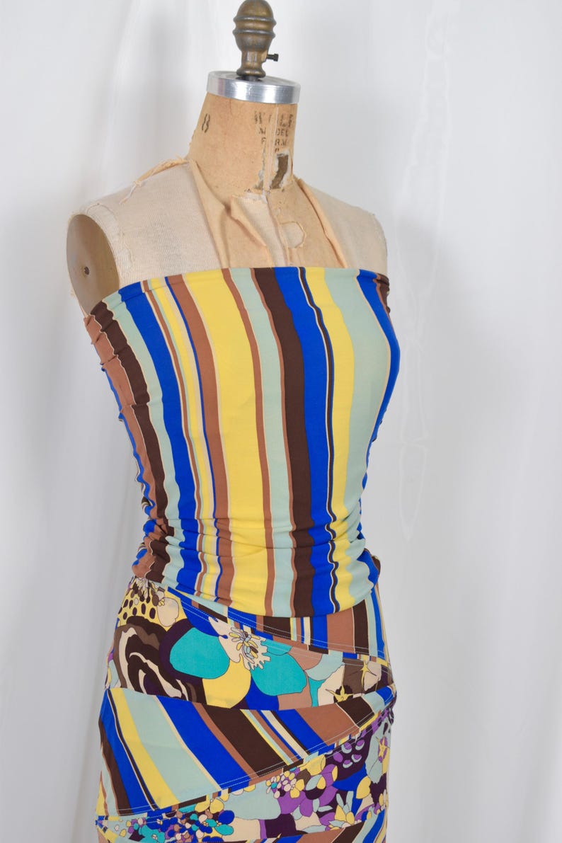 Puede incluir: Conjunto de dos piezas en maniqu&iacute;, compuesto por un top tubo y una falda. El top presenta rayas verticales en azul, amarillo, marr&oacute;n y verde. La falda tiene un colorido estampado floral y abstracto con tonos azules, morados y marrones. Dise&ntilde;o vibrante y llamativo.