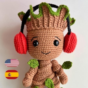 May include: A crocheted Groot doll, brown with green leaves and red earmuffs. The doll has a smiling face and black eyes. The text "I AM GROOT" is at the top. The doll is wearing headphones. The doll is handmade.