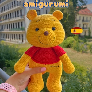 May include: A handmade Winnie the Pooh amigurumi doll. The yellow bear wears a red shirt and has a smiling face. The image includes text that says "Winnie Pooh amigurumi" and "Patron en espanol".