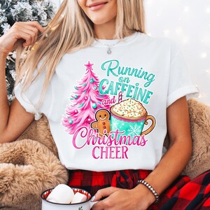 May include: White t-shirt with a colorful Christmas graphic. The design includes a pink Christmas tree, a gingerbread man, and a mug of coffee with the text "Running on Caffeine and Christmas Cheer."