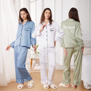 May include: Three sets of satin pajamas in blue, white, and sage green. Each set includes a button-down shirt and pants with black piping. The blue shirt has "Scarlett" embroidered, the white shirt has "Alice", and the green shirt has "Bridesmaid".