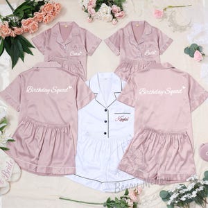 May include: A collection of matching pajama sets in pink and white, with personalized names and the text "Birthday Squad." The sets include short-sleeved button-down shirts and shorts. Also included are matching slippers and eye masks.