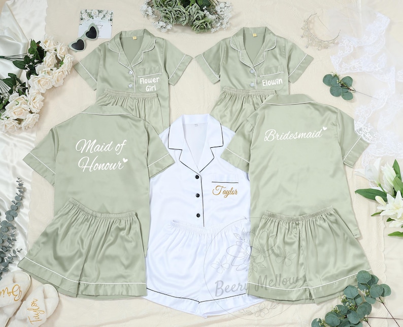 May include: A collection of matching pajama sets in sage green and white. The sets include short-sleeved button-down shirts and shorts. Some shirts are embroidered with titles like "Flower Girl," "Bridesmaid," and "Maid of Honour."