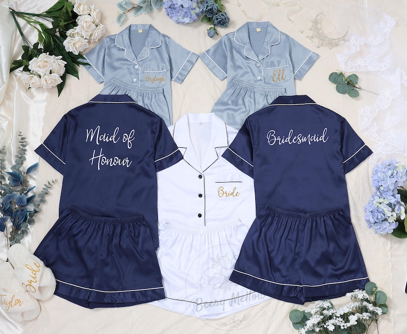 May include: Matching pajama sets in navy blue, light blue, and white, with white piping. The navy set says "Maid of Honour" on the back, and the light blue sets have names embroidered on the front. The white set says "Bride".