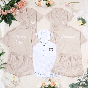May include: Beige satin pajama sets with white piping, featuring short-sleeved button-up shirts and matching shorts. Some sets are personalized with embroidered initials or titles like "Maid of Honor" and "Bridesmaid".