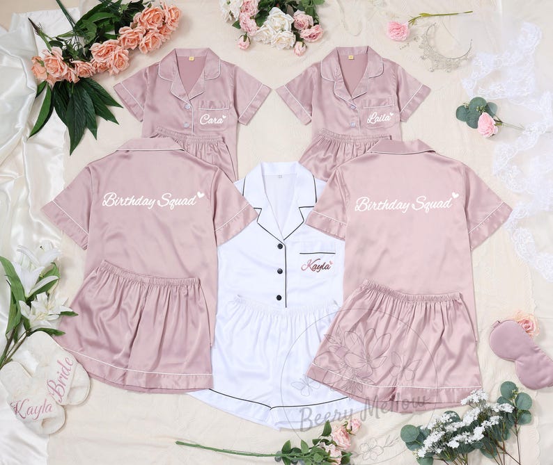 May include: A collection of satin pajama sets in pink and white. The pink sets have "Birthday Squad" printed on the back and personalized names on the front. The white set is also personalized. Matching slippers and eye masks are also included.