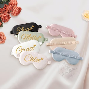 May include: A collection of satin sleep masks in various pastel colors, including black, green, white, pink, beige, and blue. Each mask is personalized with a name in gold script. The masks have elastic bands and are arranged on a white surface.