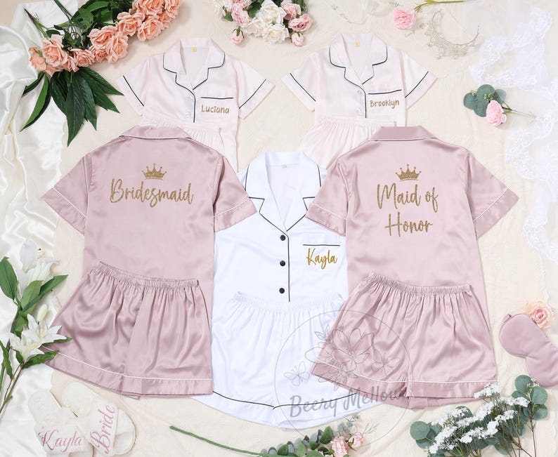 May include: Satin pajama sets in pink and white, perfect for a bridal party. The sets include short-sleeved button-down shirts and matching shorts. Some shirts are personalized with names and titles like "Bridesmaid" and "Maid of Honor".