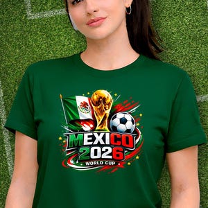 Puede incluir: Camiseta verde con el texto "MEXICO 2026 WORLD CUP", un bal&oacute;n de f&uacute;tbol, el trofeo de la Copa del Mundo y la bandera mexicana. La camiseta la lleva una persona sobre un fondo verde.