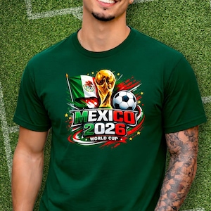 Puede incluir: Camiseta verde con un dise&ntilde;o gr&aacute;fico para la Copa Mundial de 2026 en M&eacute;xico. El dise&ntilde;o incluye la bandera mexicana, un bal&oacute;n de f&uacute;tbol y el trofeo de la Copa del Mundo. El texto "MEXICO 2026 WORLD CUP" est&aacute; presente.
