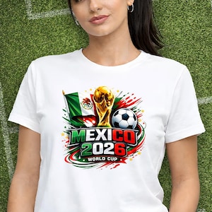 Puede incluir: Camiseta blanca con un dise&ntilde;o gr&aacute;fico colorido para la Copa del Mundo de 2026 en M&eacute;xico. El dise&ntilde;o incluye la bandera mexicana, un bal&oacute;n de f&uacute;tbol y el trofeo de la Copa del Mundo. El texto "MEXICO 2026 WORLD CUP" es visible.