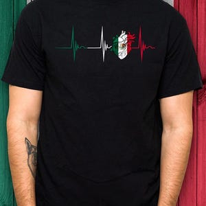 Pode incluir: Camiseta preta com um design de batimento cardíaco com as cores da bandeira mexicana. O design inclui um gráfico em forma de coração com as cores da bandeira e uma linha de batimento cardíaco em verde, branco e vermelho.