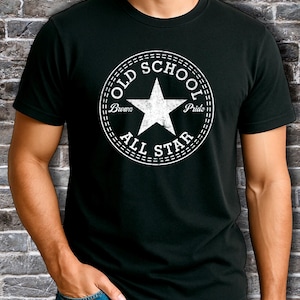 Könnte beinhalten: Schwarzes T-Shirt mit weißem Aufdruck. Der Aufdruck ist ein Kreis mit den Worten "OLD SCHOOL ALL STAR" und einem Stern in der Mitte. Das T-Shirt ist aus weichem Material.