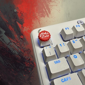 May include: A white mechanical keyboard with blue backlighting and a custom keycap. The keycap is red with the words "Nuka Cola" in white. The keyboard keys are white with blue lettering.