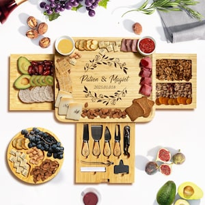 May include: A wooden serving board with a built-in drawer for cheese knives. The board is divided into sections for different types of food, including cheese, crackers, fruit, and nuts. The board is engraved with the text "Patton & Magiot 2025.01.018".