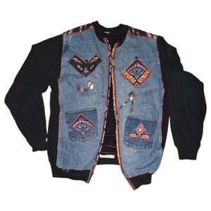 May include: A black long-sleeved sweatshirt with a denim vest overlay. The vest features colorful geometric patterns and beaded accents. The vest has two pockets and a zipper closure. The denim is faded blue.