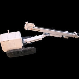 Puede incluir: Modelo blanco de perforadora sobre orugas Ingersoll-Rand. El modelo tiene un cuerpo rectangular con una sección elevada y un brazo largo y articulado. El texto "INGERSOLL-RAND" es visible en el cuerpo y el brazo. El modelo se asienta sobre orugas negras.