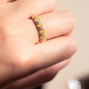 May include: A gold band ring with a row of clear cubic zirconia stones set in a geometric pattern.