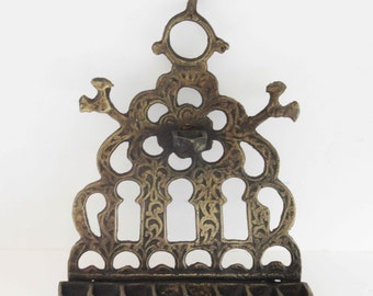 Può includere: Una menorah in ottone con un designo ornato. La menorah ha sette portacandele e uno stelo centrale con un terminale decorativo. La menorah è realizzata in un pezzo solido di ottone e ha un design tradizionale.