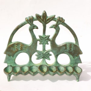 Può includere: Un portacandele in metallo color bronzo con un design a pavone. Il portacandele presenta due pavoni rivolti l'uno verso l'altro, con un elemento floreale centrale. Ha otto piccole coppe per candele e un design ad arco curvo.
