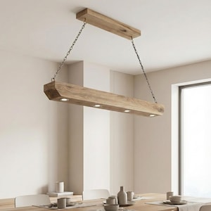 May include: A wooden rectangular pendant light fixture with five recessed lights. The light is suspended from the ceiling by two chains. The fixture is made of light-colored wood and is hanging above a dining table.