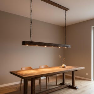 Peut inclure: Une table à manger en bois rustique avec deux chaises en bois et un luminaire en forme de poutre en bois assorti suspendu au-dessus. Le luminaire comporte plusieurs petites lumières. La pièce a une palette de couleurs neutres.