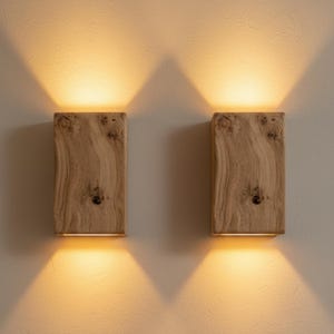 Könnte beinhalten: Zwei Wandleuchten aus Holz mit natürlicher Maserung. Jede Leuchte strahlt ein warmes, goldenes Licht aus und schafft eine gemütliche Atmosphäre. Das rechteckige Design und die nach oben und unten gerichteten Lichtstrahlen verleihen einen modernen Touch.