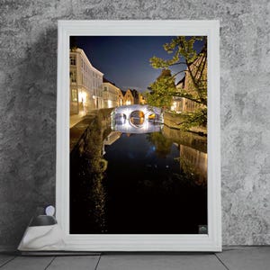 May include: A night view of a bridge over a canal in a European city. The bridge is lit up and reflected in the water. Buildings line the canal on both sides.