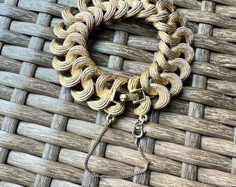 May include: Gold-toned bracelet with a textured, linked design. The bracelet features a secure clasp and a safety chain. The intricate pattern creates a bold, eye-catching accessory. This vintage-style bracelet is a statement piece.